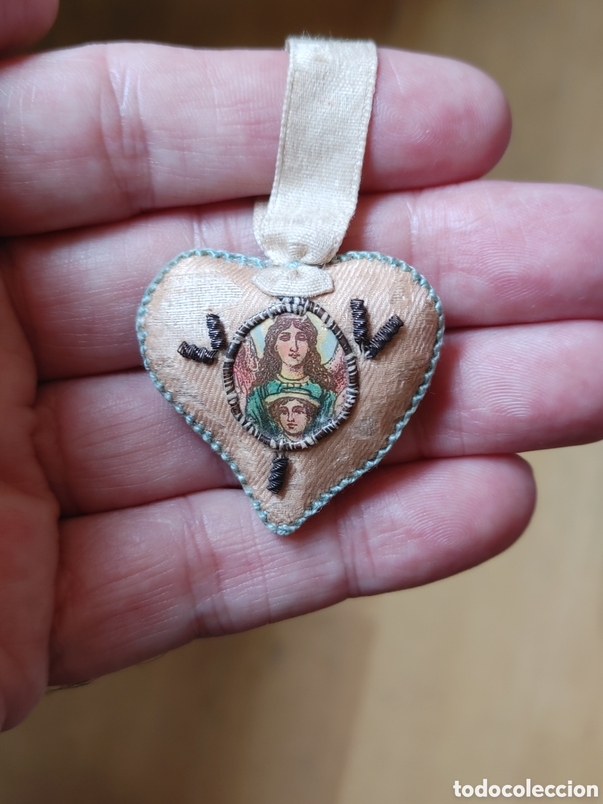 Antig&uuml;edades: Colgantito religioso. Con forma de corazon. En tela y hilo metalico.