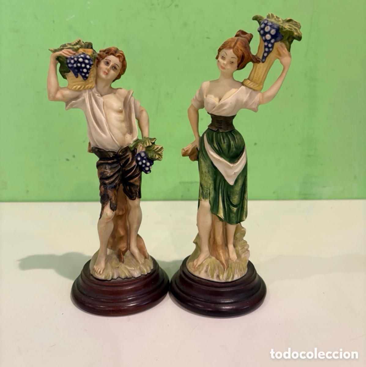 Antig&uuml;edades: Pareja de figuras decorativas de vendimiadores con racimos de uvas sobre peana de madera