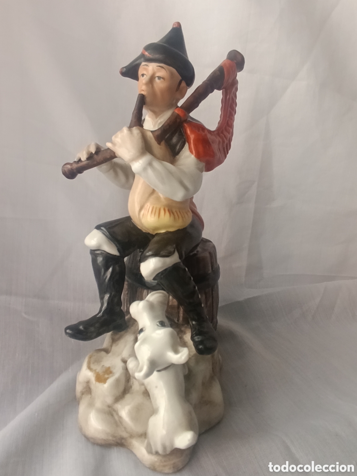 Antig&uuml;edades: Figura de Porcelana M. P. Solma (Manises) &ndash; Gaiteiro Sentado sobre Tonel con Perro (22 cm)