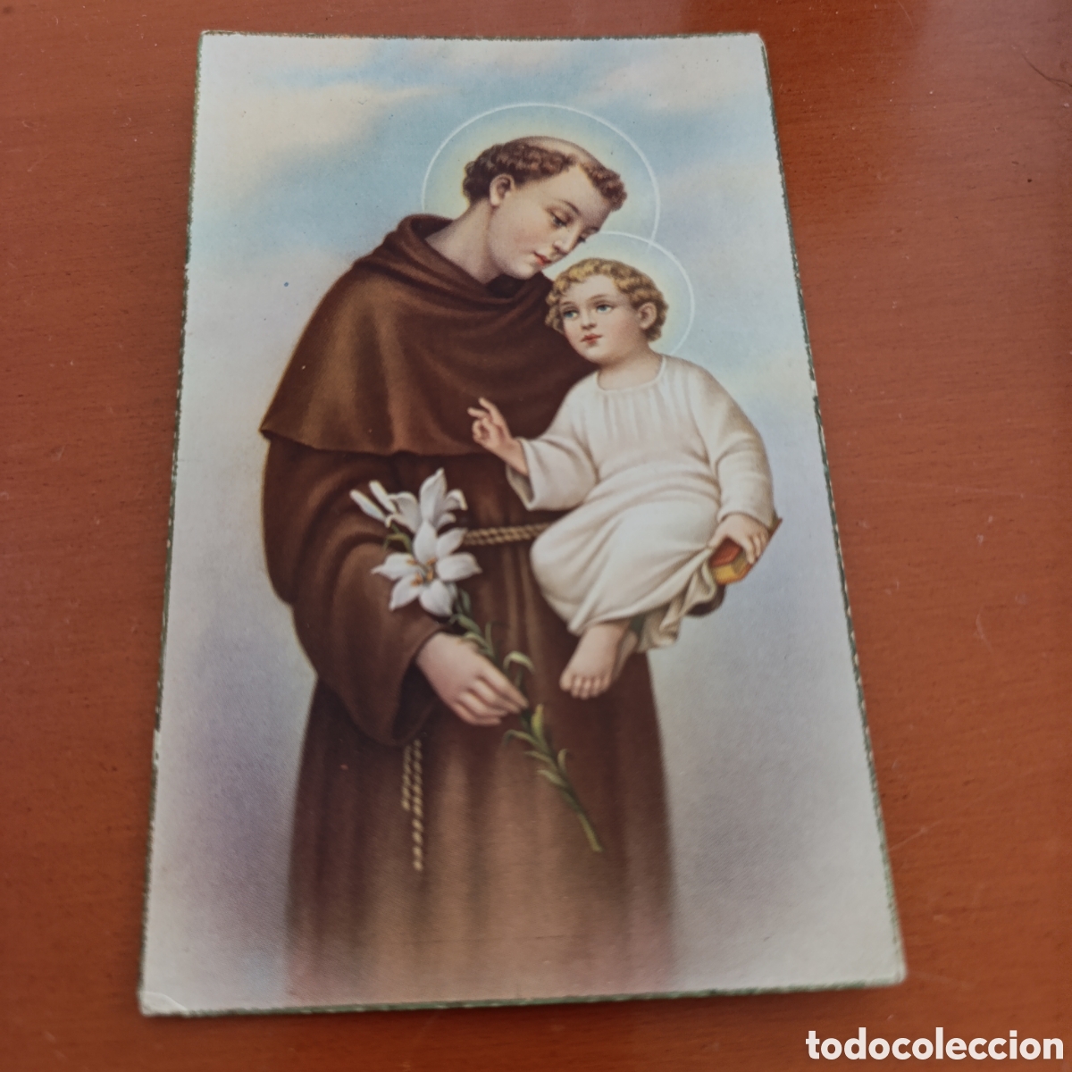 Antig&uuml;edades: Postal a&ntilde;os 40/50 San Antonio de Padua sosteniendo al Ni&ntilde;o Jes&uacute;s y una rama de lirios blancos.