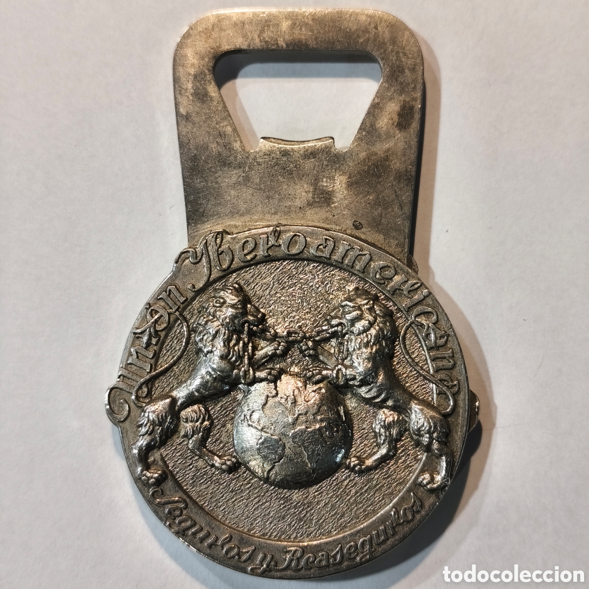 Antig&uuml;edades: Abrebotellas met&aacute;lico vintage relieve publicitario Uni&oacute;n Iberoamericana