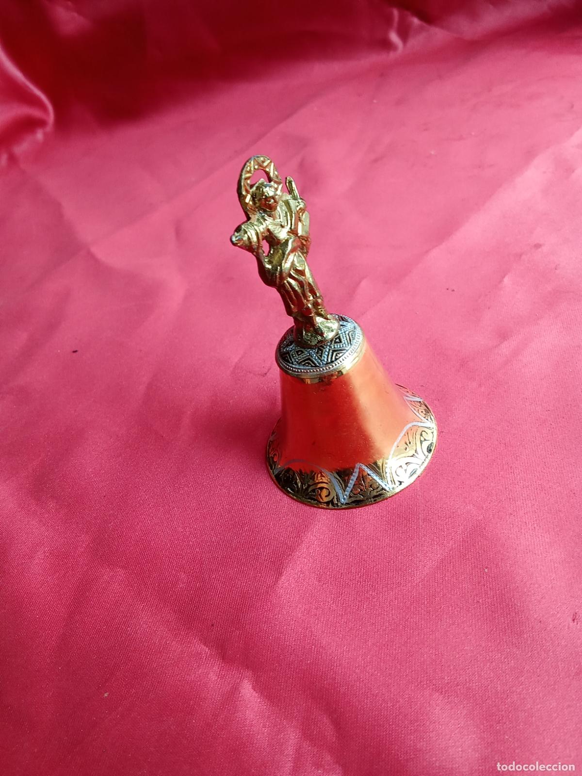 Antig&uuml;edades: Campana dorada damasquinada con santo. Vitrina juguete