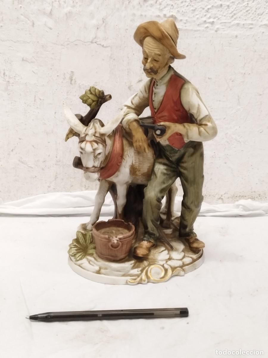 Arte: Antigua figura de porcelana hombre mayor con sombrero, chaleco rojo y pipa, con burro y cubo al pie.