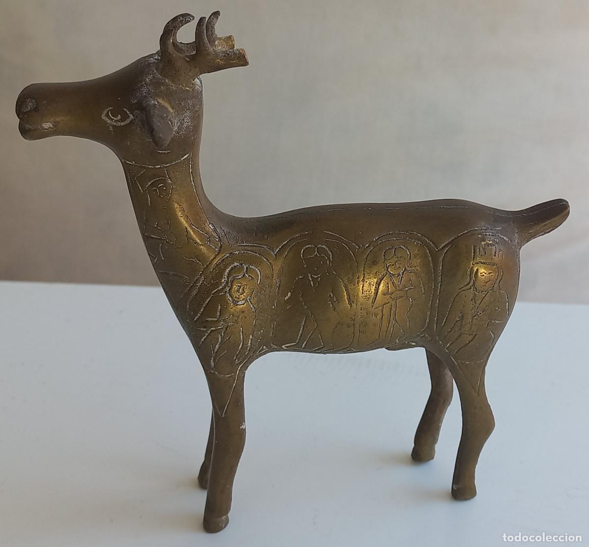 Arte: Figura de un ciervo de metal o bronce con grabados de figuras humanas en los laterales