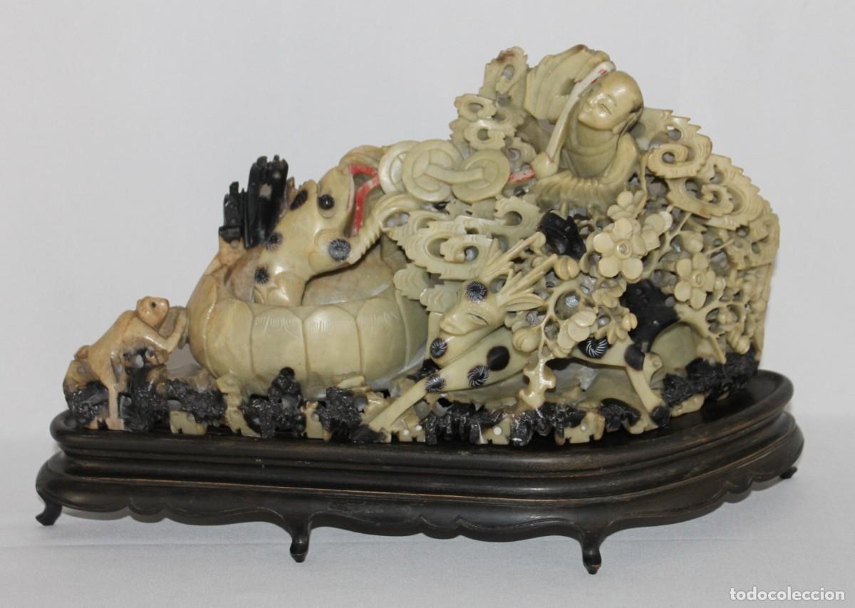 Arte: Escultura china en piedra jab&oacute;n tallada con figuras y motivos vegetales. Base de madera