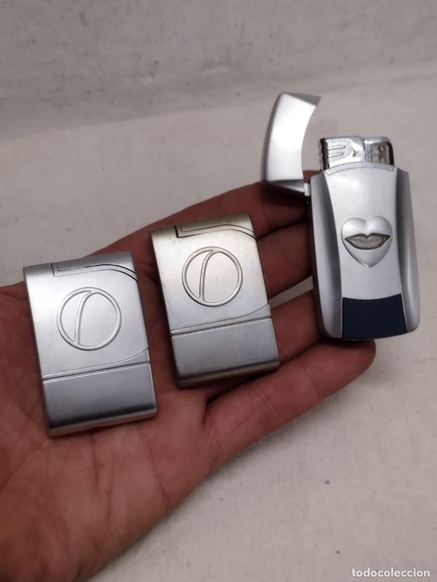 Mecheros: Lote de tres mecheros autom&aacute;ticos. Uno funcionando, de metal plateado.