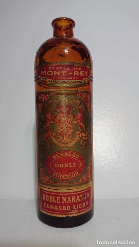 Coleccionismo de vinos y licores: BOTELLA DE VIDRIO COLOR AMBAR CON ETIQUETA DESTILERIAS MONT-REY DE BARCELONA LICOR CURASAO