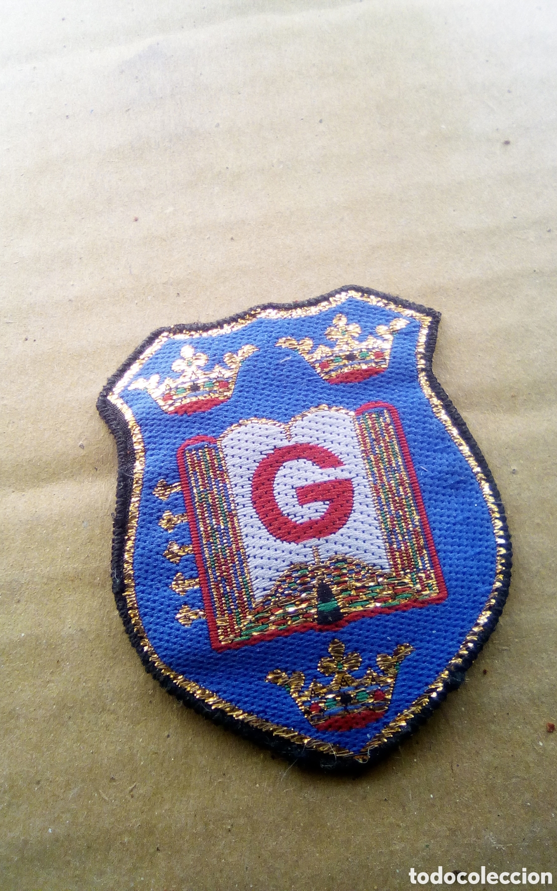 Coleccionismo: Parche de tela a identificar. Escudo con libro abierto con tres coronas y letra G en el centro. Ver.