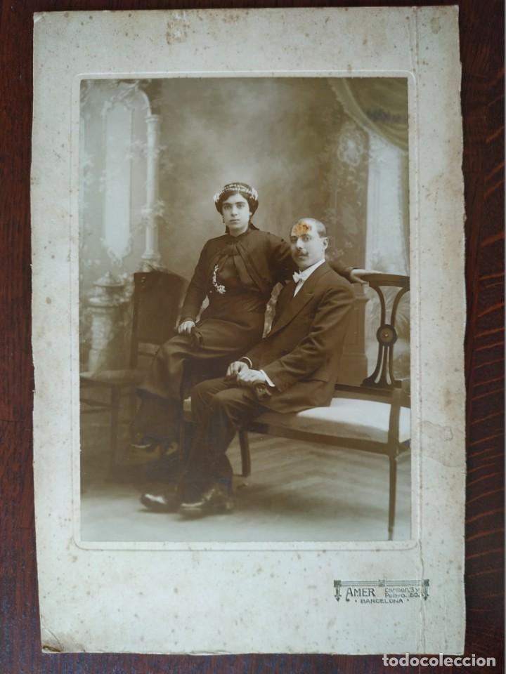 Fotografia antiga: Pareja de novios el sentado en silla y ella en reposa brazos, con fondo esc&eacute;nico mediados XIX