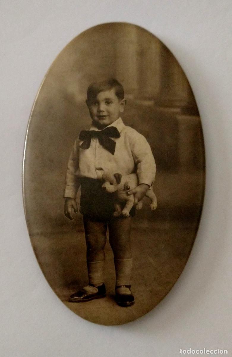 Fotograf&iacute;a antigua: Fotograf&iacute;a en metal ovalada. Ni&ntilde;o sonriente con su perrito de juguete. Peluche. A&ntilde;os 20. sv
