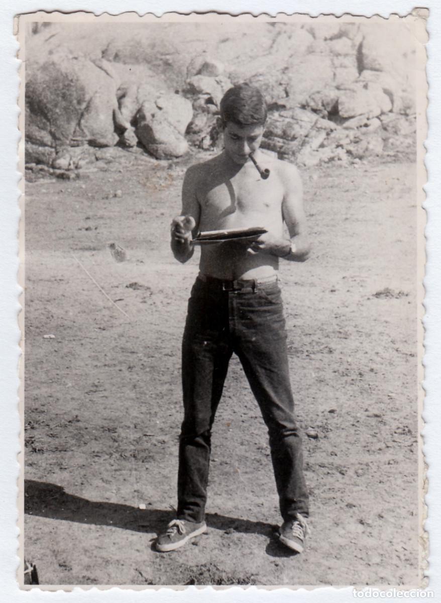 Fotograf&iacute;a antigua: Guapo chico en vaqueros fumando en pipa mientras lee una revista. A&ntilde;os 60 bm