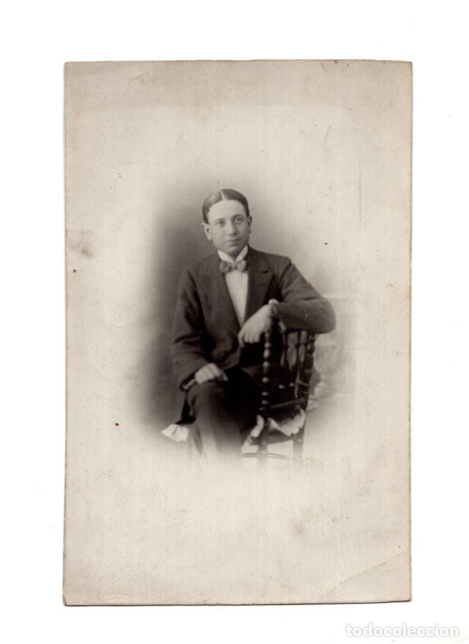 Fotograf&iacute;a antigua: UN HOMBRE JOVEN POSA SENTADO, APOYANDO EL BRAZO EN EL RESPALDO DE UNA SILLA ORNAMENTADA DE MADERA.