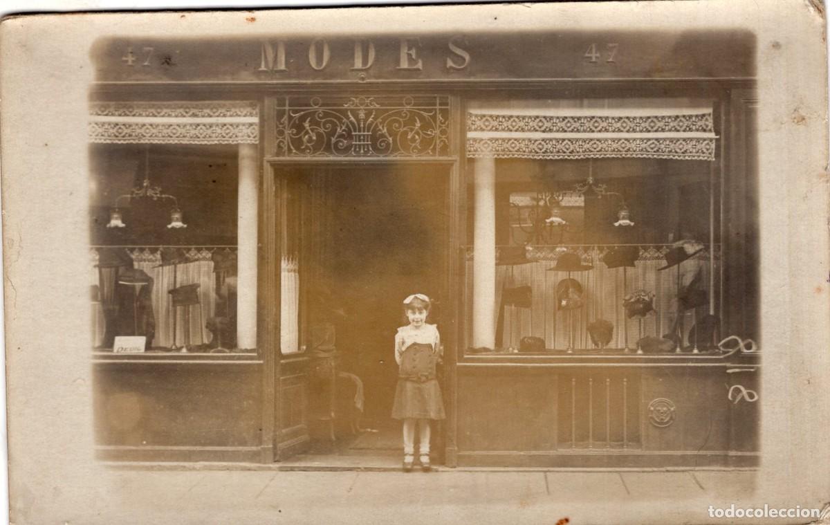 Fotograf&iacute;a antigua: Tarjeta fotogr&aacute;fica de joven posando frente a la sombrerer&iacute;a de su familia en una ciudad c.1920