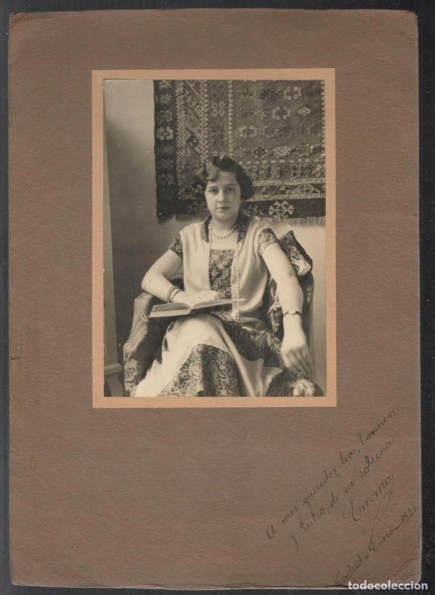 Fotograf&iacute;a antigua: Mujer sentada, vestida elegantemente, sosteniendo un libro abierto. Con tapiz al fondo. 1926