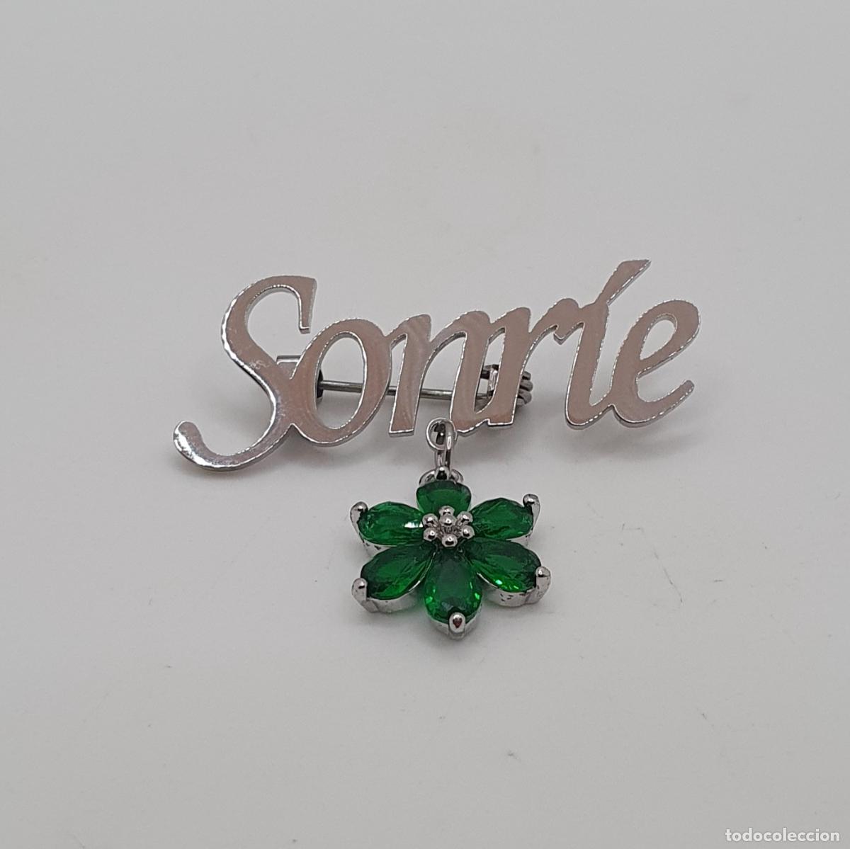 Joyeria: Hermoso broche con la palabra SONR&Iacute;E en metal plateado con dije de flor de esmeraldas creadas.