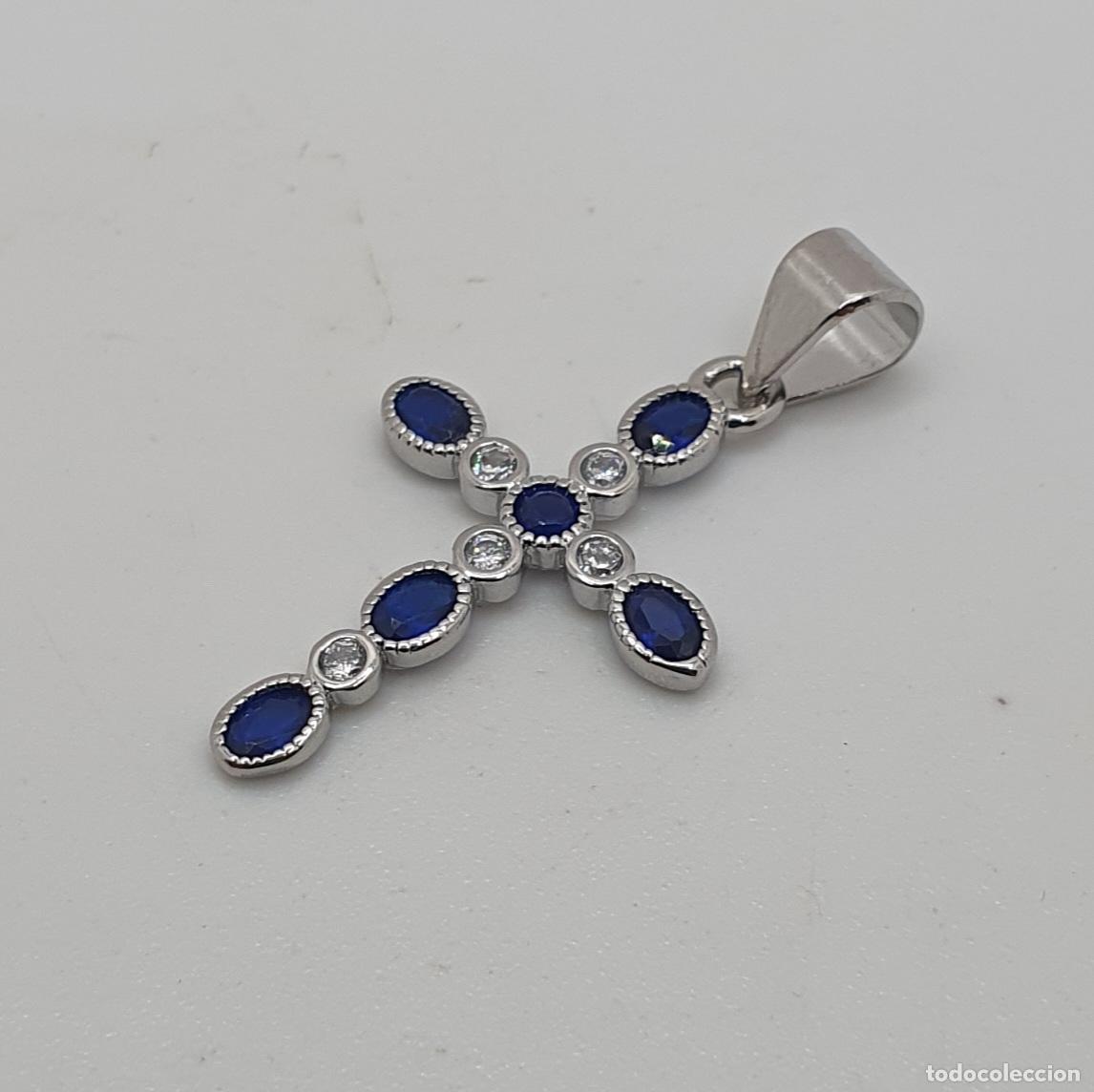 Joyeria: Elegante colgante de cruz chapada en oro blanco de 18k, circonitas y zafiros creados talla oval.