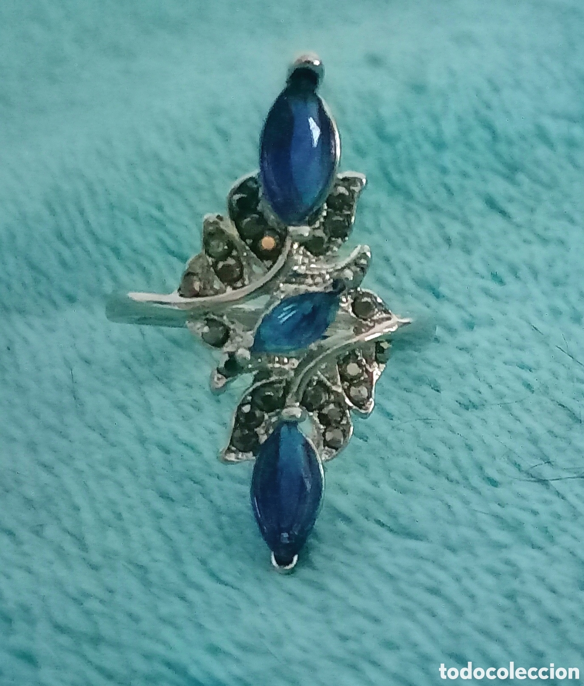 Joyeria: Original anillo plateado alargado con incrustaciones y tachuelas brillantes azul y gris. 18mm di&aacute;m.