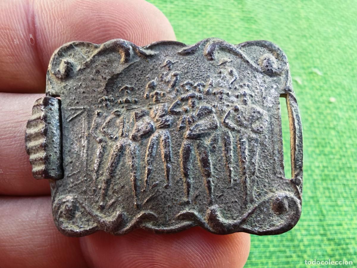 Militaria: hebilla antigua con un relieve que parece representar un grupo de figuras humanas o danzantes.