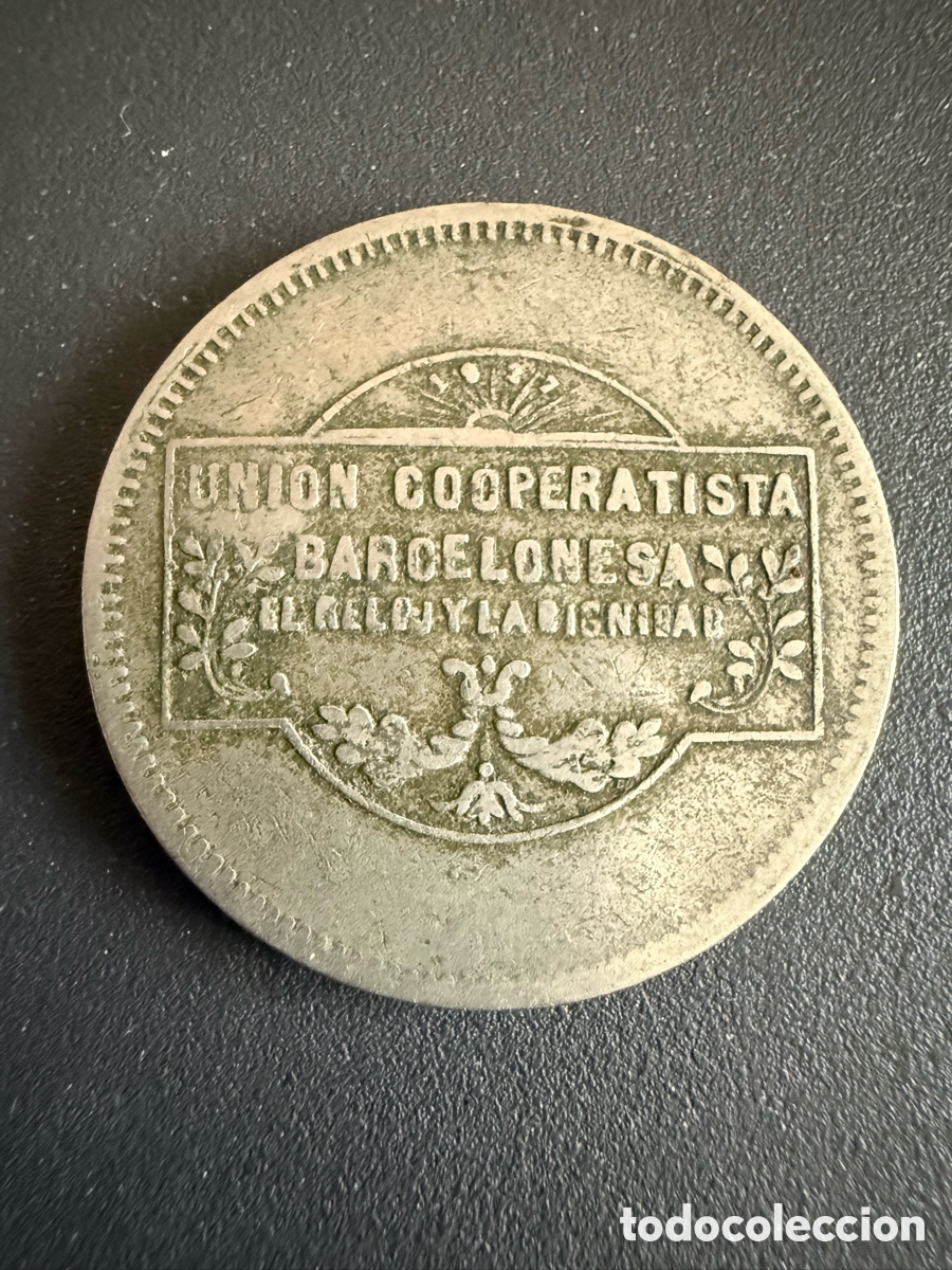 Monedas locales: Ficha Uni&oacute;n Cooperativista Barcelonesa El Reloj y La Dignidad valor 5 pesetas con resello.