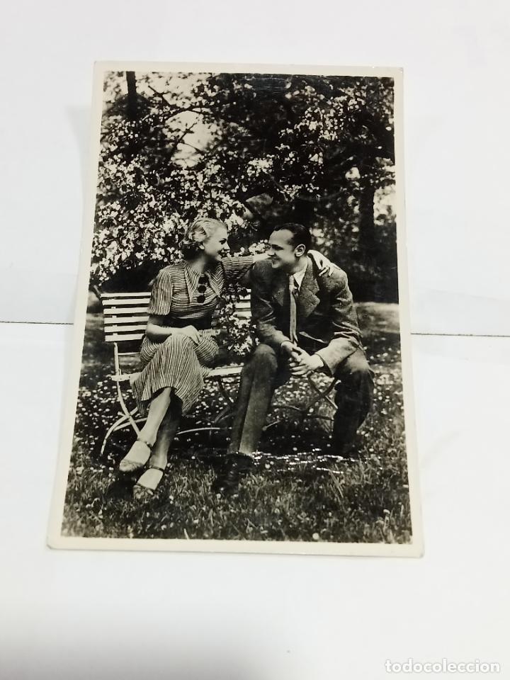 Cartoline: TARJETA POSTAL. PAREJA DE J&Oacute;VENES ENAMORADOS EN BANCO Y RODEADO DE RAMILLETES DE FLORES