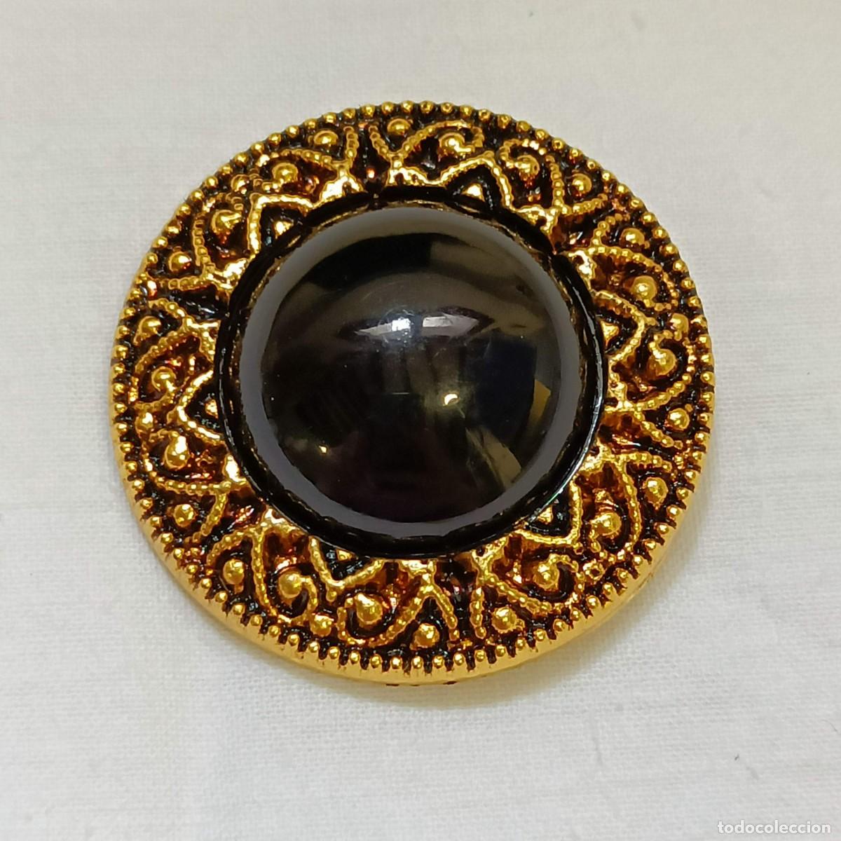 Vintage: Grande bot&oacute;n de resina imitando metal dorado, bordes tallados, cabuj&oacute;n negro, de pie. 3,7 cm.